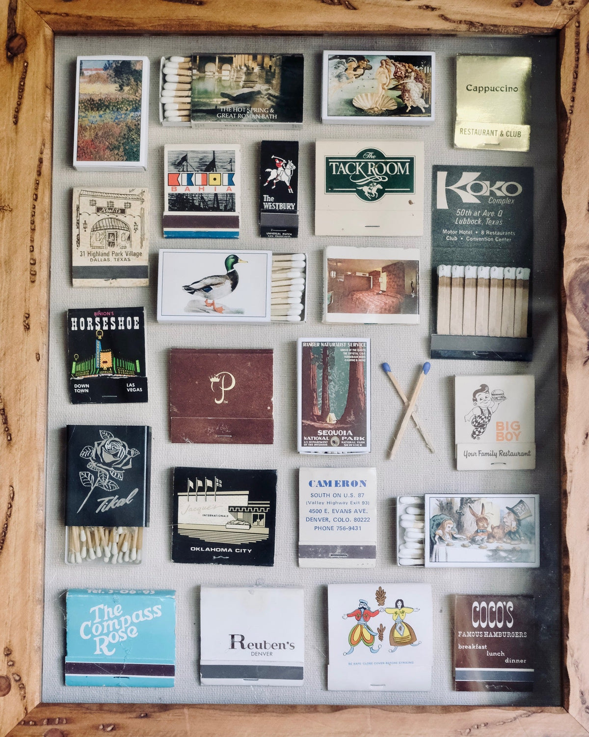 A rustic wooden shadow box display filled with vintage matchbooks, matches, and a small K&H matchbox set, photographed from above on a weathered wood surface.