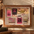A framed collage of vintage matchbooks, matchsticks, and small decorative items displayed on a wooden surface against a textured wall. The framed piece includes visible text such as 'Grége Encantados', 'Alive & Cookin'', 'Latin Casino', 'Reno Spa Grand Flaminco', and 'Thank You'.